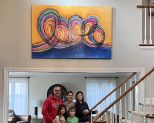 family posing in front of the final painting hung on their wall.